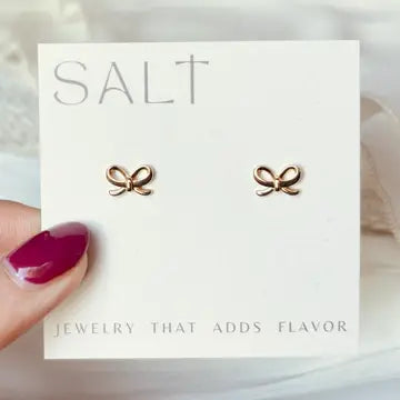 Gold bow shaped earrings are pictured on cardstock held by a hand.